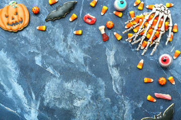 Tasty Halloween candy corns, skeleton hands and cookies on blue background