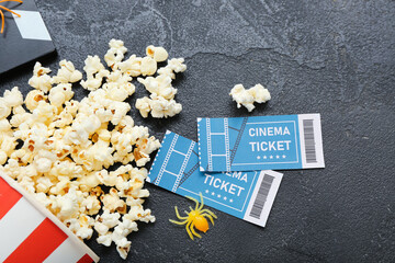 Bucket with tasty popcorn, spider and cinema tickets on dark background, closeup. Halloween celebration