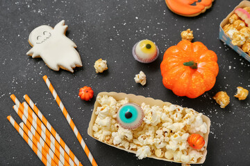 Paper box with tasty popcorn, cookie and candies on dark background, closeup. Halloween celebration