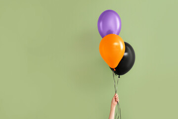 Female hand with different Halloween balloons on green background