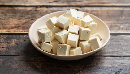 Bowl of raw tofu cubes on rustic wooden background