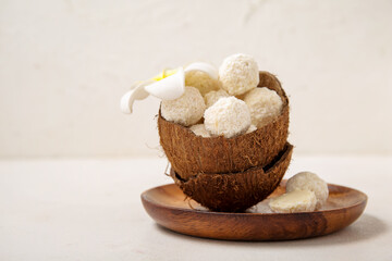 Coconut shell with white chocolate candies and plumeria flower on light table