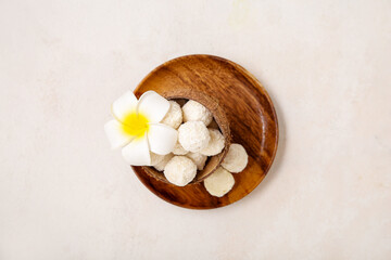 Coconut shell with white chocolate candies and plumeria flower on light table