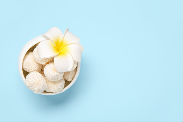 Fototapeta na wymiar White chocolate candies with coconut topping and plumeria flower in bowl on blue background