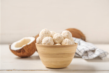 Wooden bowl with tasty coconut candies on white table