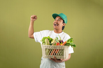 Photo asian young man farmer holding a crate full of fresh vegetables isolated on green background