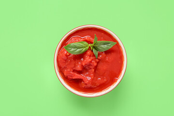 Bowl with canned tomatoes on green background