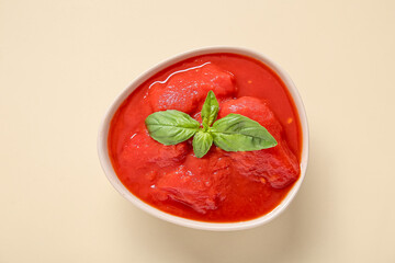 Bowl of tasty canned tomatoes with basil on color background