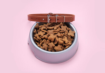 Bowl of dry pet food and collar on pink background
