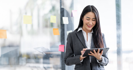 Image of young asian woman smiling and holding digital tablet, standing in office, copy space.