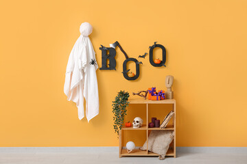 Shelving unit with Halloween decor, ghost and text BOO hanging on orange wall in room