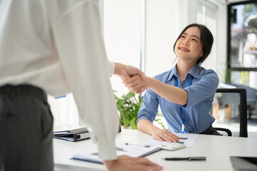 A friendly Asian female HR recruiter is shaking hands with a candidate after an interview