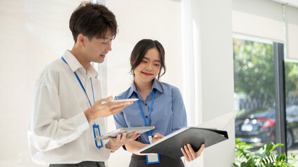 A friendly Asian male worker is explaining and helping a female colleague with a project