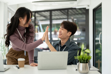 Cheerful Asian business people give high fives to each other to celebrate their successful project
