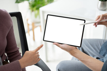 A businesswoman discussing and showing some details on a tablet to a male colleague.