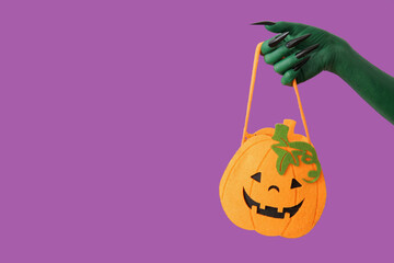 Green hand of witch with bag on purple background. Halloween celebration