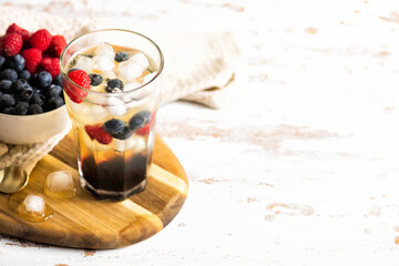The glass of iced tea with berries on the wooden table.