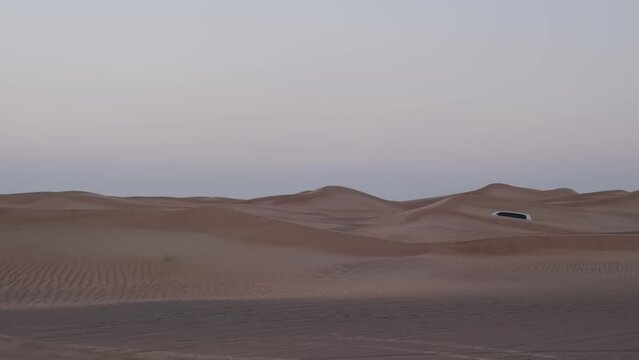 A caravan of white off-road vehicles rides through the sand dunes of the desert
