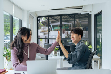 happy Asian female office worker gives high fives to a male colleague, celebrating project success