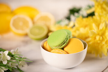 Green and Yellow macron in a bowl, lemon and limes in the background. Also flowers in the background.