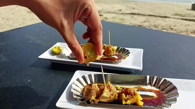 Hand squeezing calamansi juice over pork siomai, a traditional Filipino snack while enjoying the sunny weather at the beach