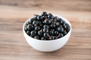 Fresh black currant on in a white bowl. Handful of berries on the wooden table.