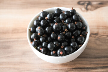 Fresh black currant on in a white bowl. Handful of berries on the wooden table.