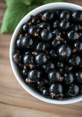 Fresh black currant on in a white bowl. Handful of berries on the wooden table.