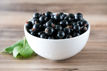 Fresh black currant on in a white bowl. Handful of berries on the wooden table.