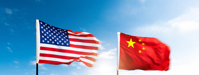 USA and China flags against blue sky background