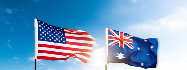 USA and Australia flags against blue sky background