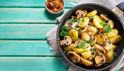 Fried potatoes with mushrooms, onions and parsley served in a frying pan with turquoise wooden...