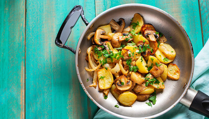 Fried potatoes with mushrooms, onions and parsley served in a frying pan with turquoise wooden background