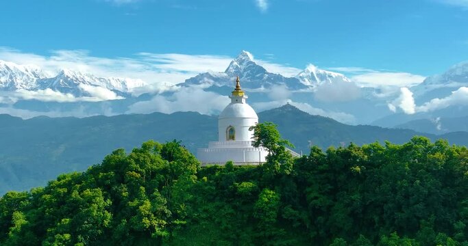 Aerial view of Peace Pagoda stupa in Pokhara Nepal. Surrounded by Beautiful mountain ranges and landscapes, Stupa stands still between the green forest. Peaceful place to meditate. 4K