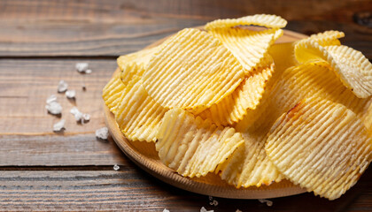 Corrugated potato chips and salt on wooden background. Close up