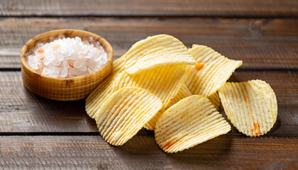Corrugated potato chips and salt on wooden background. Close up