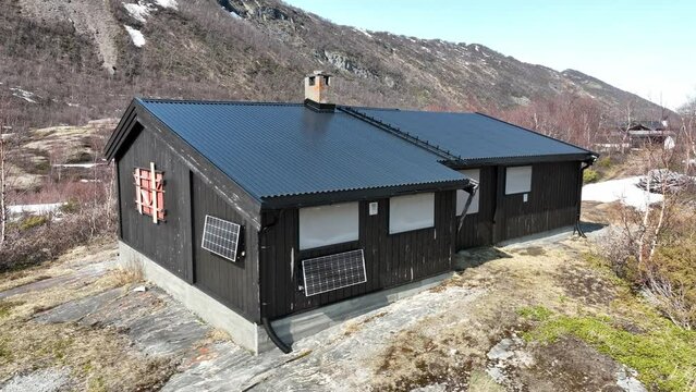 Closed off small traditional mountain cottage in Norway mountain - Springtime sunny day with solar panel on wall and mountain background