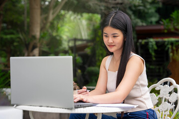young attractive asian woman working over laptop at resting zone in the resort garden during travel on vacation, concept of digital nomad,travel freely,working remotely on internet online