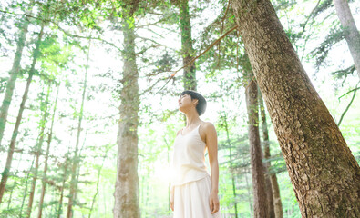 新緑の美しい森で深呼吸をしている健康的な女性/森林浴	