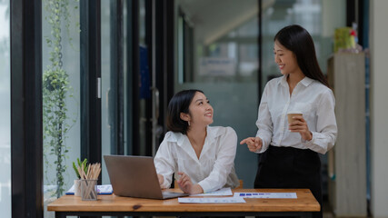 Two young Asian businesswoman consult and talk analysis of marketing planning with laptop computer.