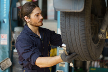 mechanic worker checking car replacing car wheel and tyre in auto repair shop store service. worker maintenance examining and installing wheel tire at garage.