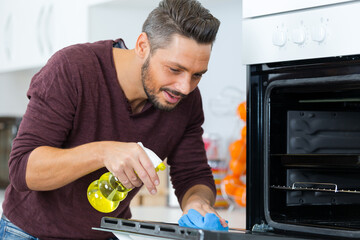 happy young man in overall cleaning oven