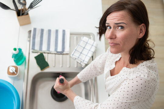 young woman unblocking sink in kitchen