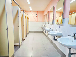Row of public toilet, restroom, lavatory, water closet and white ceramic wash basins and large mirrors in public restrooms.	