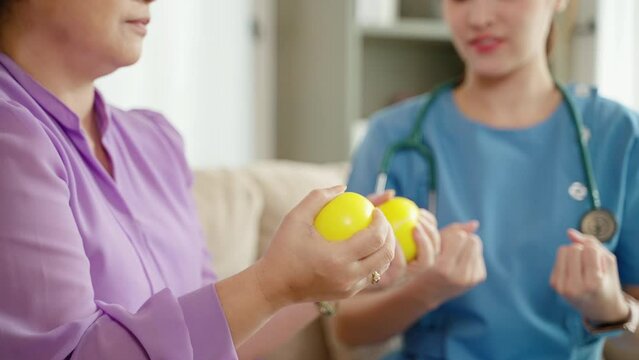 Nurse or caregiver helping elderly person with physio with hand squeezing ball, healthcare concept
