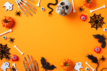 Happy Halloween concept. Frame made of skull, bats, spider webs, bones, ghosts, bloody eyes on orange background. Flat lay, top view, copy space.