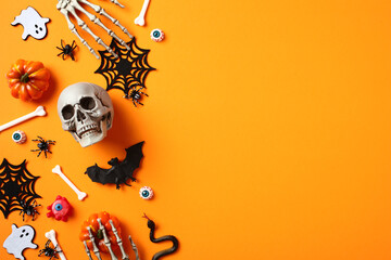 Halloween flat lay composition with skull, spiders, pumpkins, ghosts, skeleton hands on orange background.