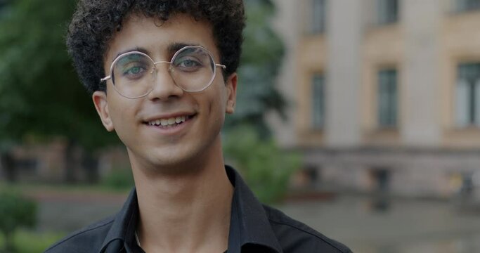 Slow motion portrait of Middle Eastern man wearing glasses smiling outdoors in city. Positive emotion and cheerful person concept.