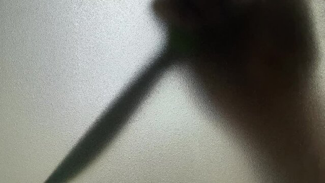 Male hand silhouette shadow behind translucent mirror holding knife moving slowly 
