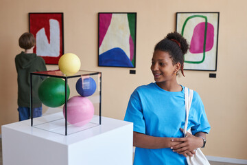 Colorful portrait of smiling teenage girl looking at abtract sculpture in modern art gallery